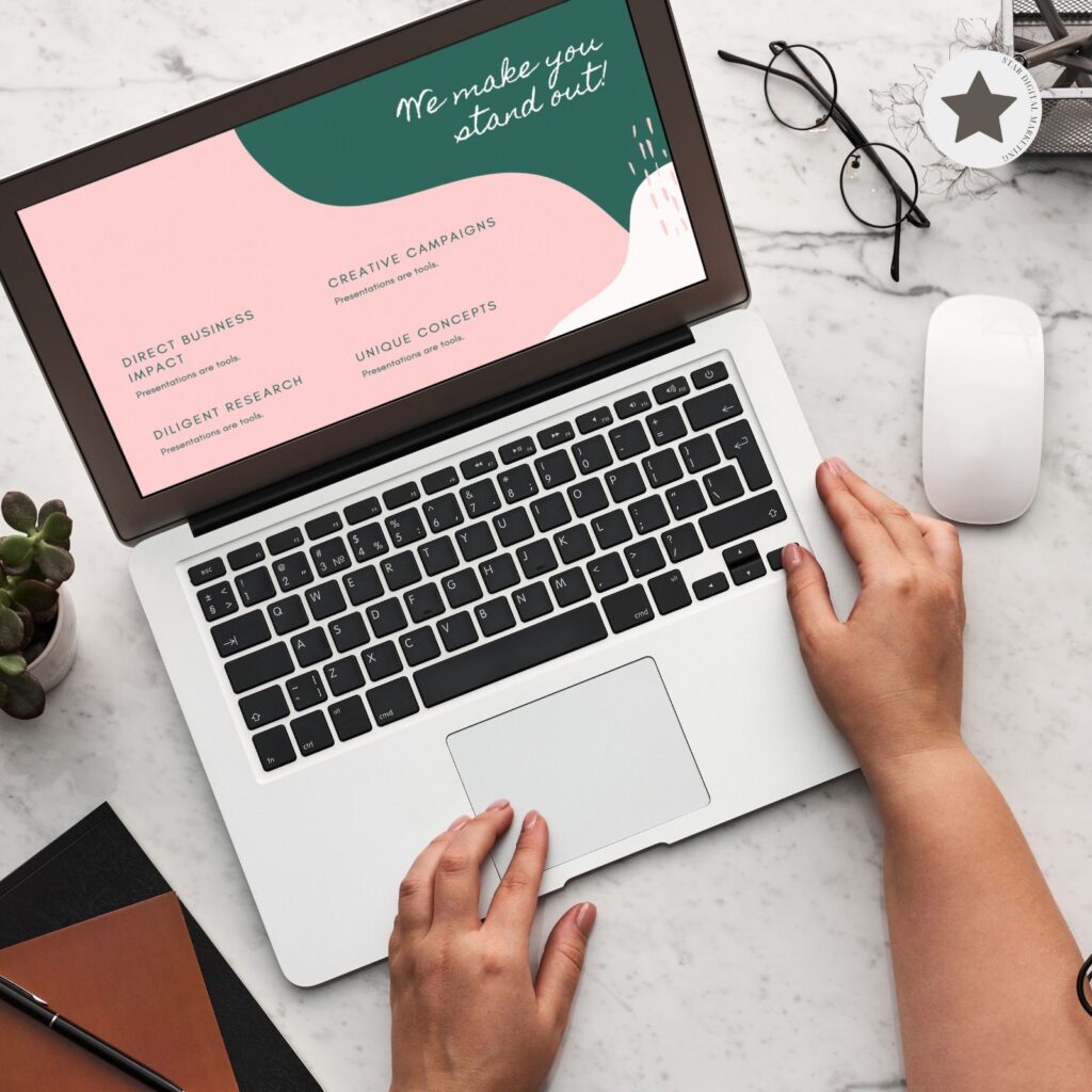 Person working on laptop with marketing presentation on screen, glasses and plant beside it.